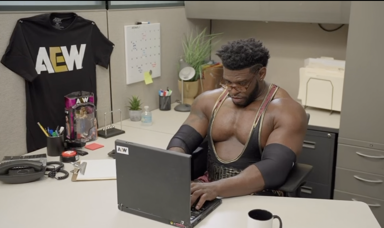 AEW wrestler working at a laptop in an office cubicle