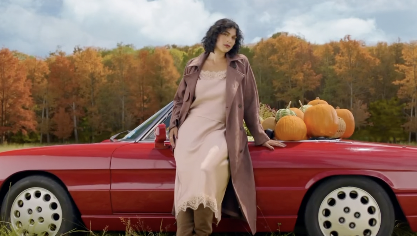 Woman beside a red car and pumpkins in an autumn landscape